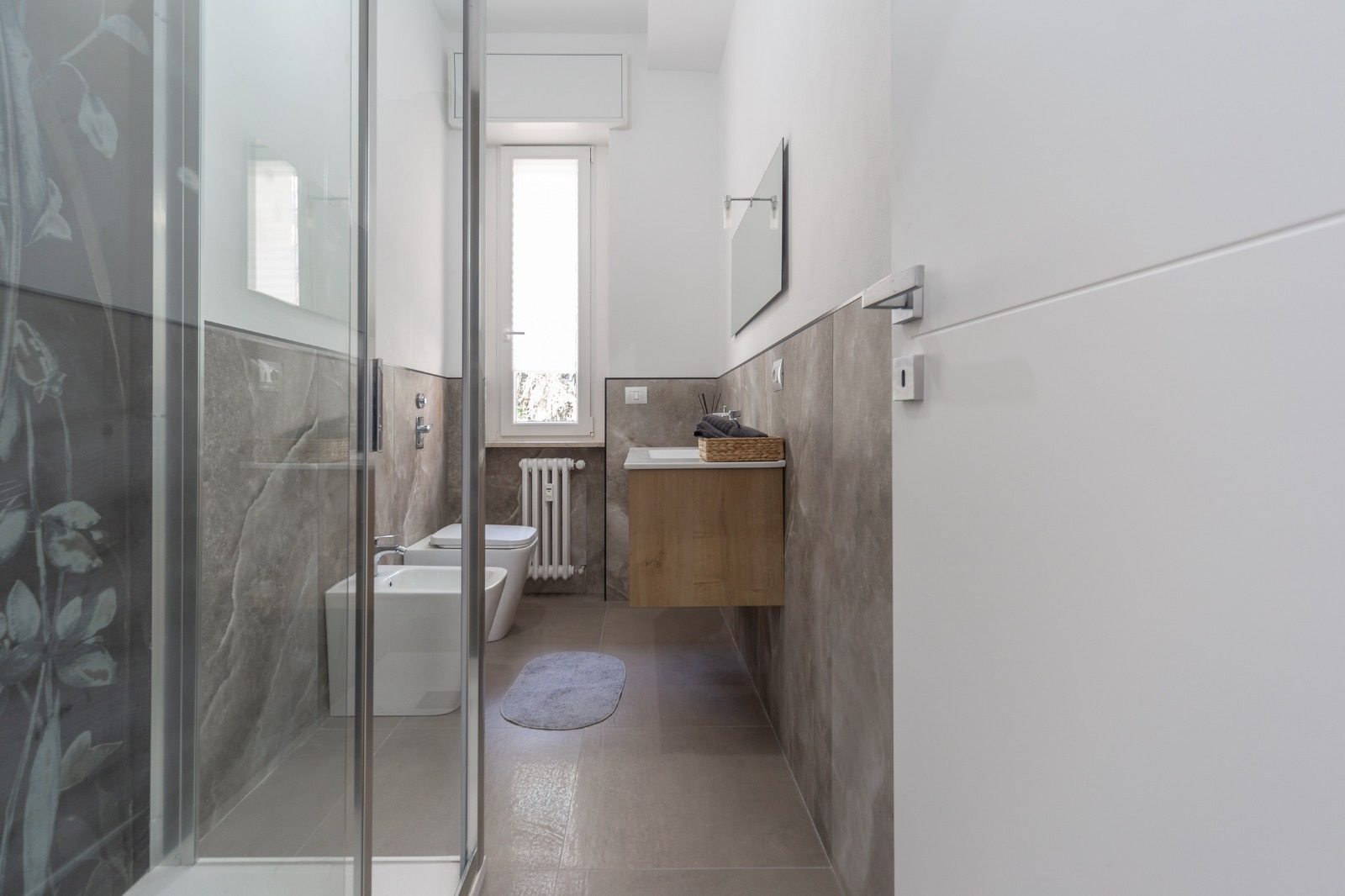 Bagno finito con box doccia in cristallo e rivestimento in gres effetto pietra