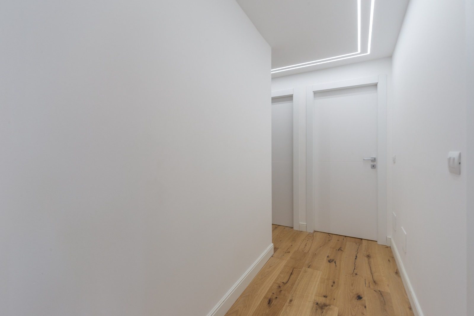 Corridoio con porte bianche a filo muro e illuminazione lineare a LED nel controsoffitto
