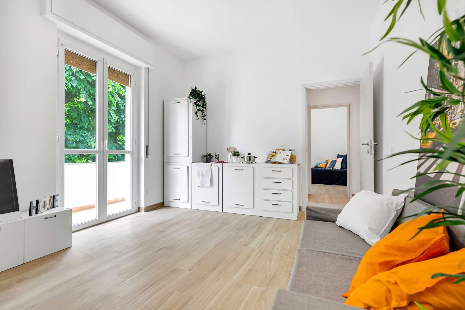 Zona giorno con cucina lineare bianca, portafinestra sul balcone e porta aperta sulla camera