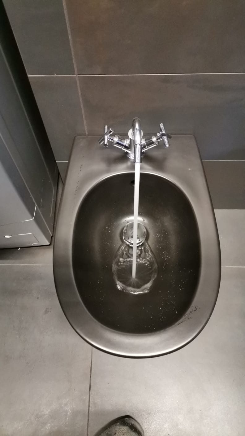 Bidet sospeso scuro con rubinetteria cromata a croce e getto d'acqua aperto nel catino