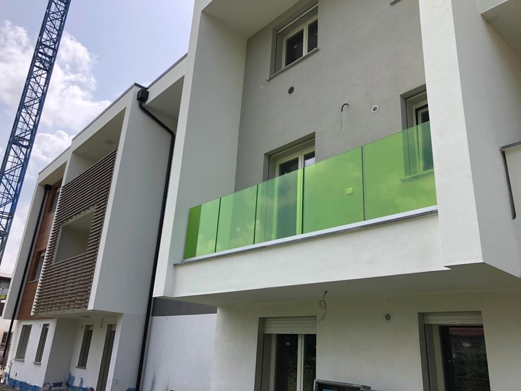 Balcone con parapetto in vetro verde su palazzina nuova, gru di cantiere sullo sfondo