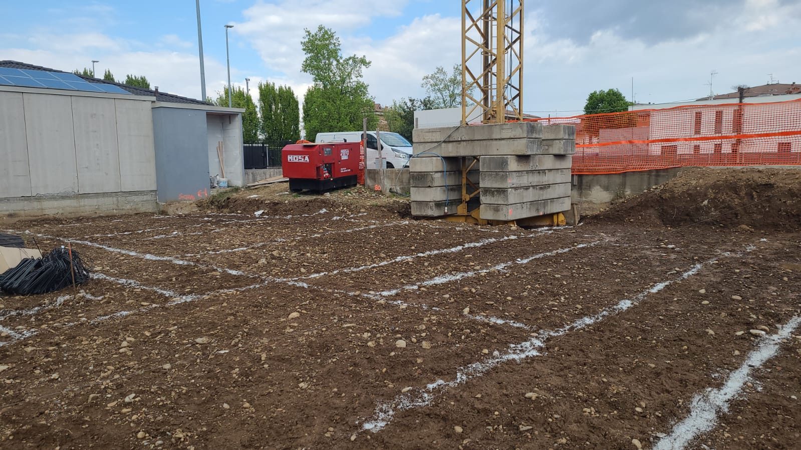 Cantiere con tracciamento a calce sul terreno, gru a torre zavorrata, recinzione arancione e gruppo elettrogeno