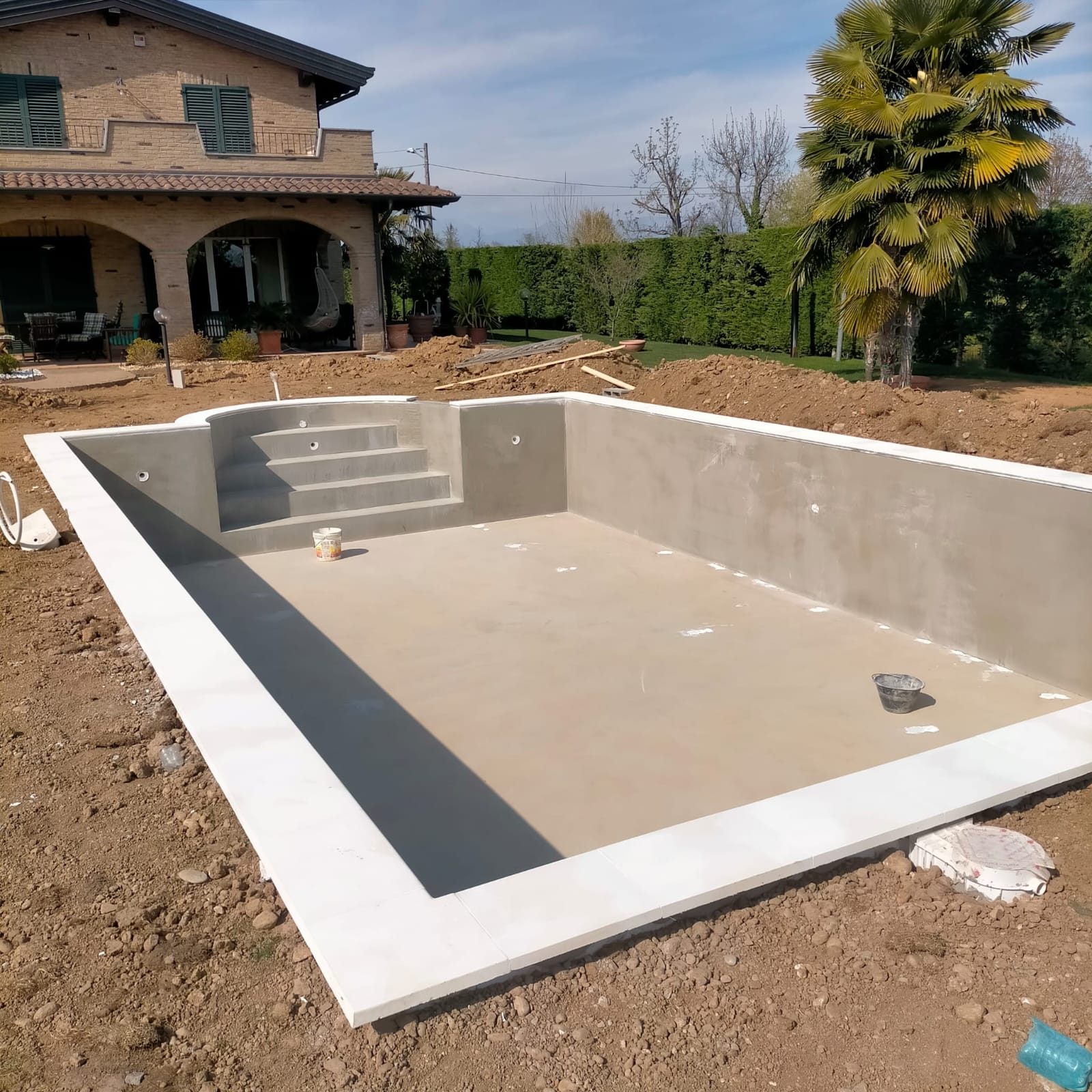 Vasca di piscina interrata rifinita in cemento, con scala interna a gradoni e bordo perimetrale chiaro
