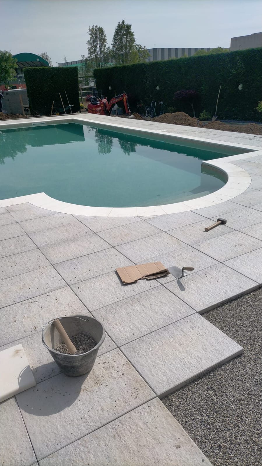 Piscina piena d'acqua con bordo curvo e posa in corso delle lastre di pavimentazione esterna