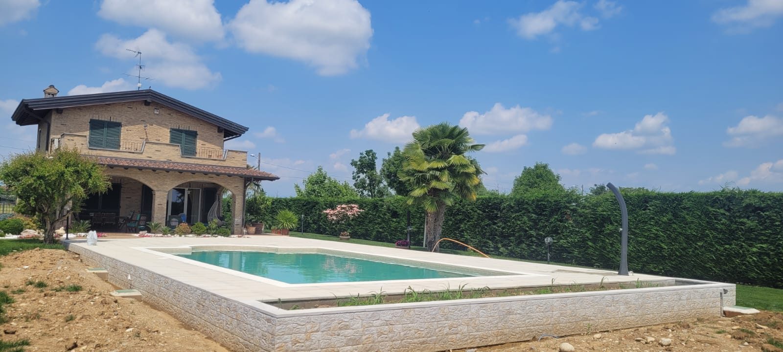 Vista d'insieme della piscina completata davanti alla villa, con pavimentazione perimetrale e muretto in blocchi