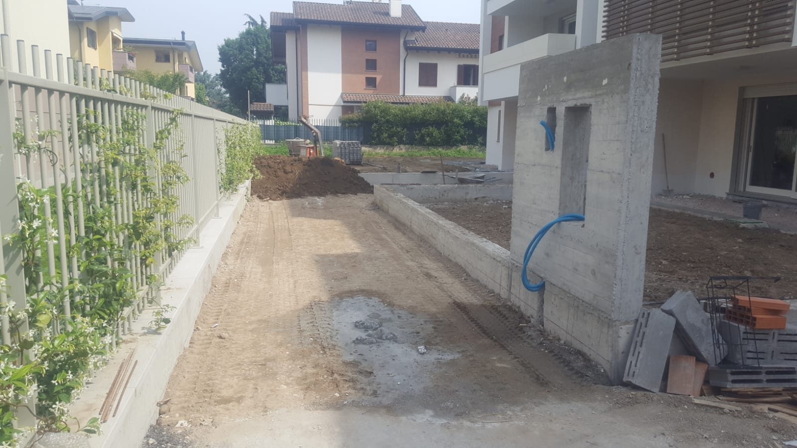 Passaggio carrabile sterrato tra recinzione e muro in cemento armato con cavidotto blu a vista