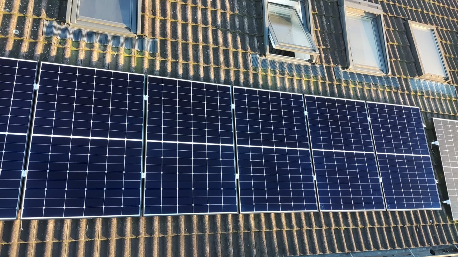 Moduli fotovoltaici allineati su falda in tegole di cemento, accanto a finestre da tetto