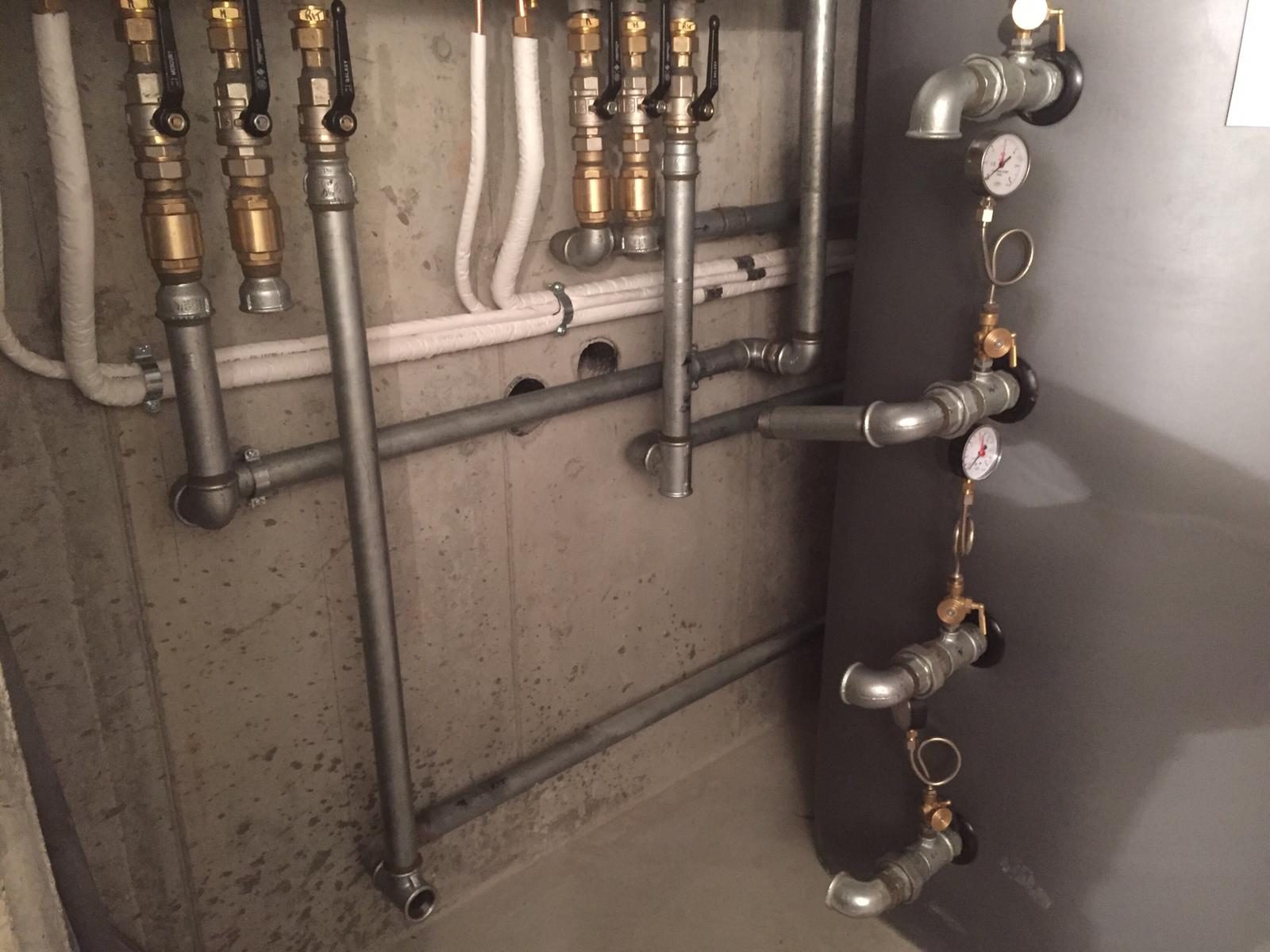 Locale tecnico con tubazioni in acciaio zincato, valvole a sfera, manometri e serbatoio grigio a destra