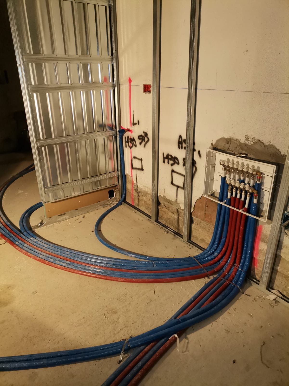 Cantiere interno con tubi multistrato rossi e blu dal collettore incassato e orditura metallica per cartongesso