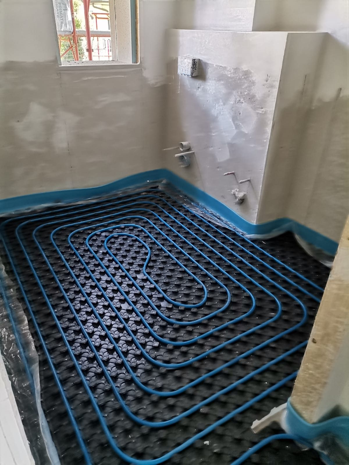 Tubazioni blu del riscaldamento a pavimento posate su pannello bugnato, con fascia perimetrale blu