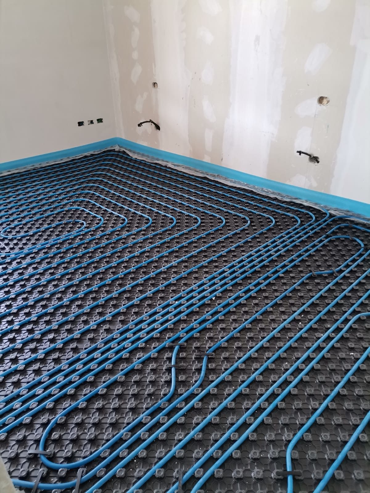 Stanza con pannello bugnato nero e tubi blu del riscaldamento a pavimento posati a serpentina